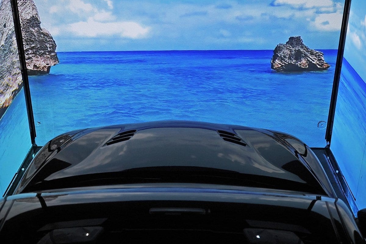 Schwarzes Auto von innen gesehen mit offenem Panoramadach, Blick auf blaues Meer mit Felsen und blauem Himmel