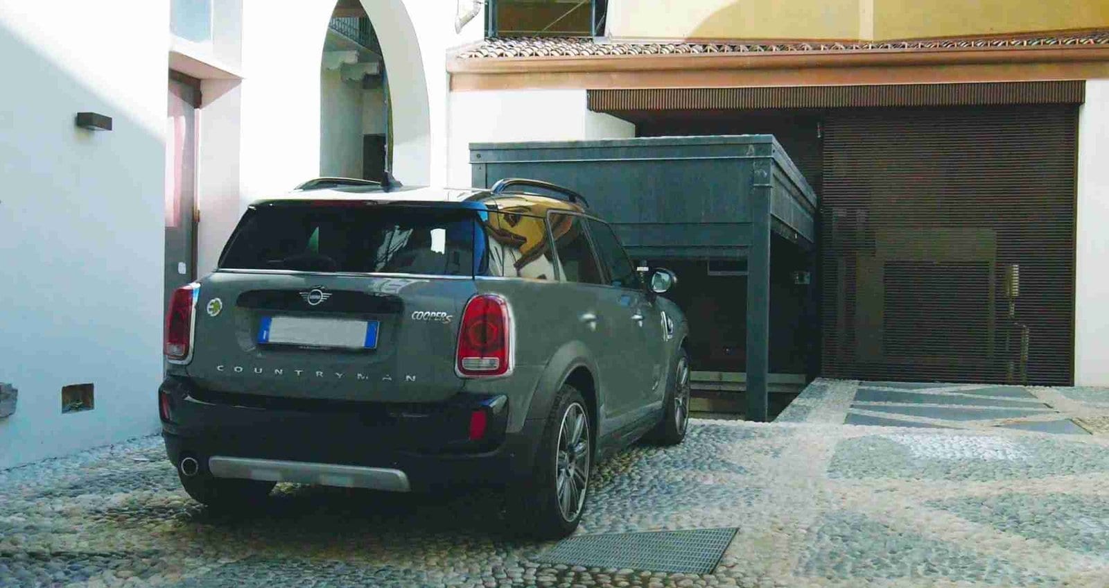 Grünes Auto vor grüner Metallstruktur geparkt, Hof mit Wohngebäuden im Hintergrund