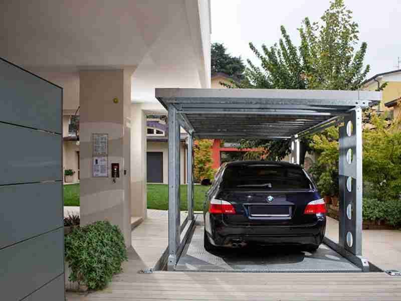 Autoaufzug Ohne Fahrer an Bord System - Schwarzes Auto unter grauer Metallstruktur mit Dach geparkt, in Wohnumgebung mit Garten